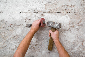 Young adult man hands using sledgehammer, metal stone chisel and removing old concrete on floor. Closeup. Point of view shot. Preparing for repair work of home. Flooring restoration. Top down view. - obrazy, fototapety, plakaty