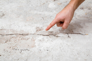 Young adult man hand finger pointing to cracked concrete floor. Building problem and solution...