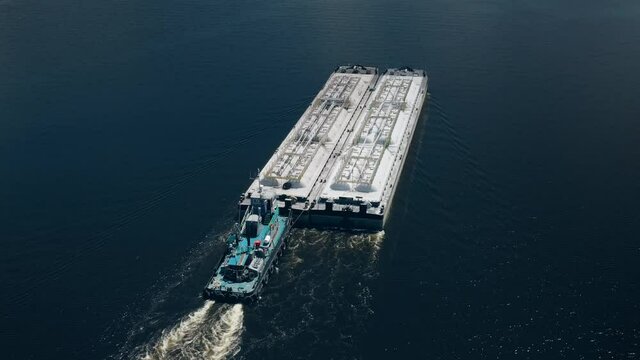 Aerial river tugboat barge transports cargo goods closeup. Gas and oil logistics transportation industry. Freight transport floats on calm water. Delivery cargo to port, shipping. Cinematic drone shot