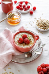Oatmeal with the addition of fresh raspberries served in a pink cup on a table covered with a white linen tablecloth. top view. A healthy breakfast or dessert