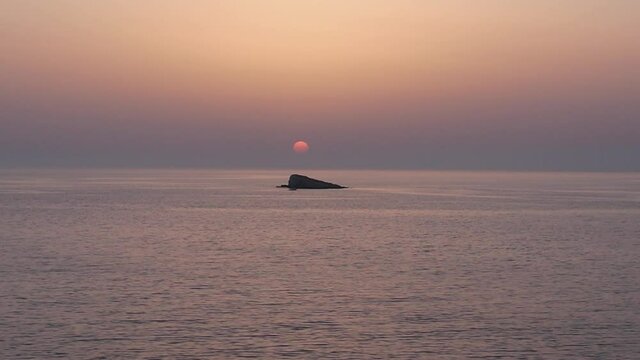 Plan de drone minimaliste au dessus de la mer avec le coucher de soleil en arri&egrave;re-plan et un petit bateau qui passe