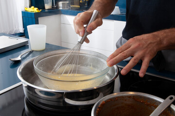 Cocinero  haciendo crema pastelera al baño María con varillas. Chef making custard in a bain-marie with whisks