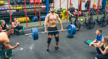 Strong man practicing weightlifting in a fitness center with his partners cheering him on