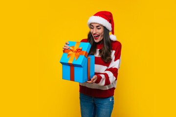Close up photo of beautiful excited smiling woman with Christmas gift box in hands is having fun while posing on yellow background