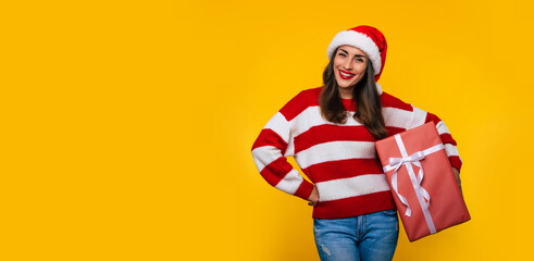 Close up photo of beautiful excited smiling woman with Christmas gift box in hands is having fun while posing on yellow background