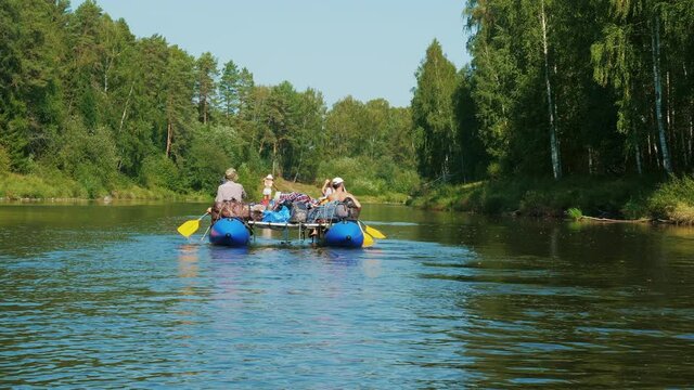 Tourists float down river on catamaran. Sunny day, summer, forest. Men and women rowing oars on raft. Water recreation. Rafters paddle. Sportive weekend, vacation. Hobby, lifestyle