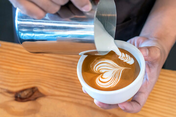 Closeup image of male hands barista pouring milk make coffee latte art in coffee shop