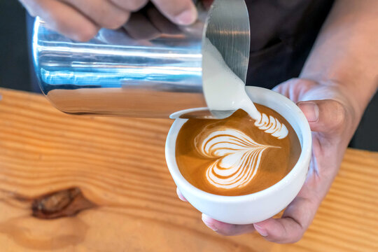 Closeup image of male hands barista pouring milk make coffee latte art in coffee shop