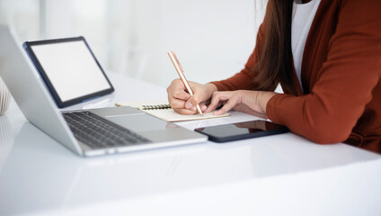 focus on hand young asian businesswoman holding pen writing note book while she using laptop and digital tablet working or meeting online