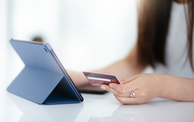 Focus on hand young asian woman holding mock up of creditcard and using digital tablet to shopping or paying online