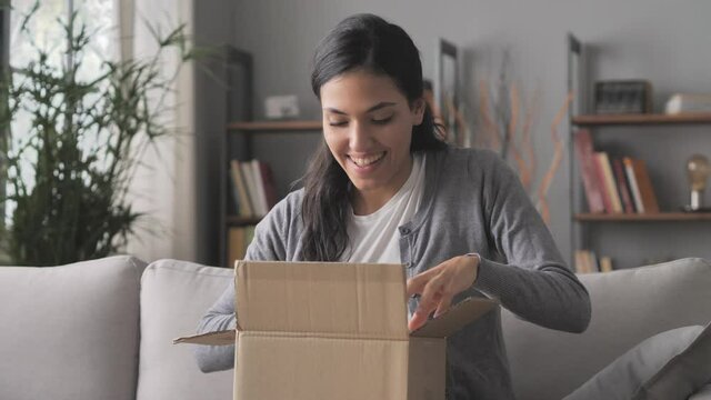 happy young woman on sofa opening online purchase box package,female consumer sits on couch opens postal parcel,home delivery shipping concept