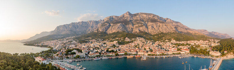 Drone aerial view of Makarska city, Croatia. Sunset over the city, beach and se. Biokovo mountains in the background. Summer time.