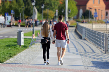 Para młodych ludzie, kobieta i mężczyzna spaceruje deptakiem, chodnikiem we Wrocławiu.	
