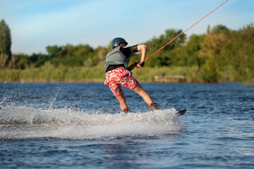 Fototapeta premium Teenage boy wakeboarding on river, back view. Extreme water sport