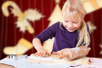 little smiling girl using cookie cutter on dough to make christmas cookies in front of christmas...