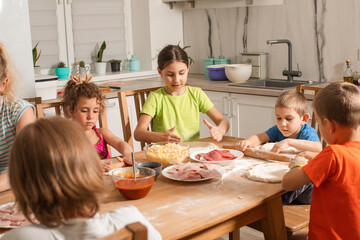 Happy kids sit at a table in the kitchen and make pizza