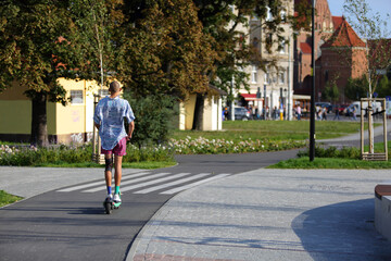 Młody mężczyzna jedzie na hulajnodze elektrycznej po ścieżce rowerowej.