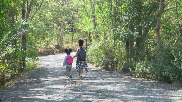 African american cute little sisters hiking in a forest . Two black girl on field trip in nature . Group of school children with backpack holding hand together walking in park .