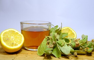 Photo of herbal and linden tea inside the glass pot together with linden tea leaves and broken and not broken walnuts on the wood table.