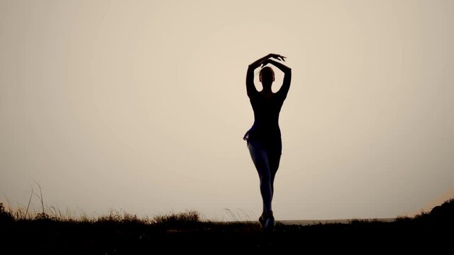 the silhouette of a woman at sunset dancing gracefully ballet. elegant smooth swings of the hands