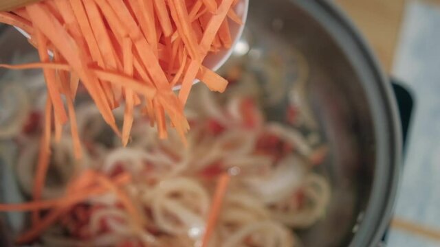 Adding spoon of grated yam and carrots to pot with onion and tomato slices