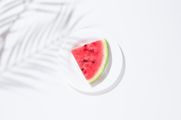 Slice of watermelon on a white plate on a white table. Top view, flat lay