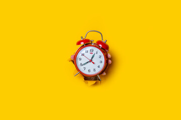 Hand holds a red watch in a hole in a torn yellow background