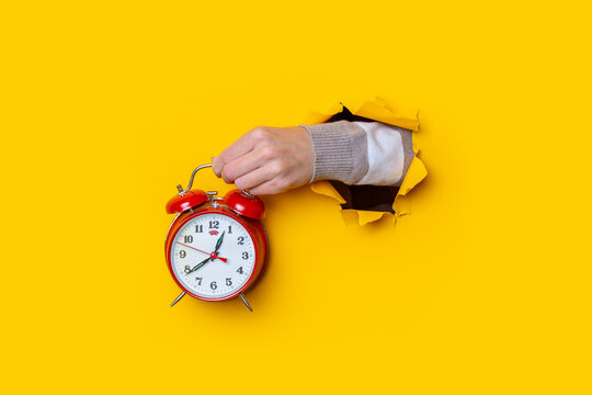 Female Hand Holding A Red Watch In A Hole On A Yellow Background