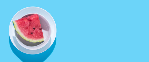 Slice of juicy red watermelon in a plate on a blue background. Top view, flat lay. Banner