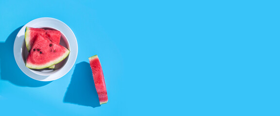 Slices of red watermelon in a plate on a blue background. Top view, flat lay. Banner