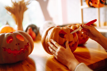 Close up of woman hands with knife carving pumpkin. On the table lies a orange pumpkin with a painted horrible face. Halloween, decoration and holidays concept.