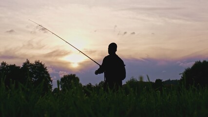 Fototapeta na wymiar Silhouette of Adult Male Trying to Catch a Fish using Spinning Technique with Carbon Fiber Fishing Rod in Rays of Sun during Sunset 