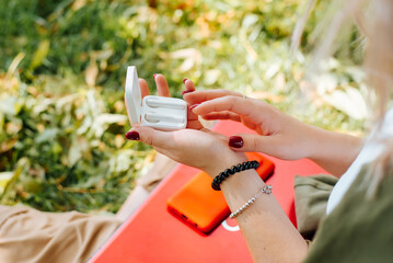 Close-up of young woman and wireless earphones outdoors. Selective focus on female hands holding...