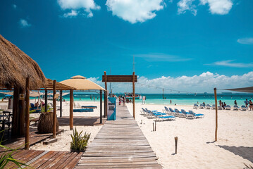 Cancun, Mexico. May 30, 2021. Wooden pier leading from sand into sea with moored yachts or sailboat on water surface. Tourists holidaying at beach
