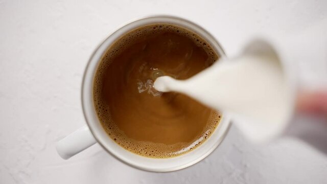Adding cream to a cup with black, hot coffee placed on white table