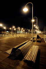 Fototapeta na wymiar Night view of benches illuminated by street lamps on the dock of the port of genoa, Liguria Italy, Europe.