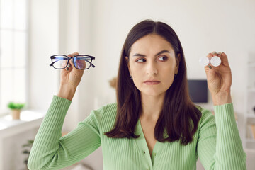 Headshot portrait of woman choosing between glasses and eye lenses. Serious beautiful Caucasian...