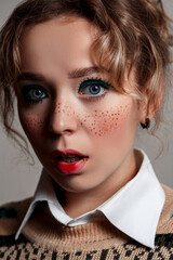 portrait of a young beautiful blue - eyed girl . with painted freckles and a cheerful make-up, she is surprised. on a gray isolated background.