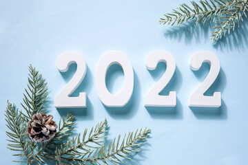 Happy New Year. White wooden numbers 2022, green branches fir tree, cone on blue background . Greeting card. Top view, flat lay.