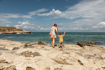 Mom and child at the sea. A girl and her son are looking at the sea. Rocky seashore. The family is traveling.