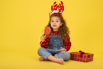 Little girl for the Christmas holidays with a gift and a lollipop on a yellow background to copy  space