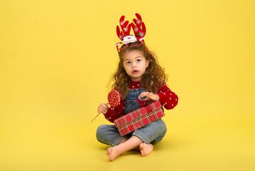 Little girl for the Christmas holidays with a gift and a lollipop on a yellow background to copy  space