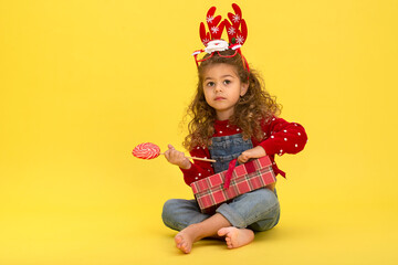 Little girl for the Christmas holidays with a gift and a lollipop on a yellow background to copy  space