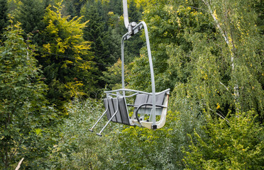 Emtpy chairlift in ski resort station, temporarily closed during summer season. With green trees...