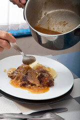 Manos de cocinero poniendo salsa sobre carne con patatas.  Cook hands putting sauce on meat with potatoes