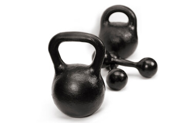 Kettlebells of 24 and 32 kg and dumbbells of 5 kg on a light background, focus on lighter weights....
