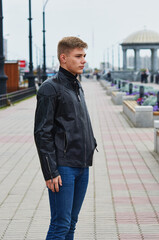 Handsome brutal blond man in black leather jacket model style. Portrait of a handsome guy on a blurred urban background with a rotunda. 