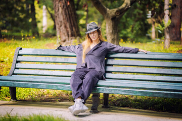 Obraz premium A long-haired woman in lilac clothes and a hat sits on a park bench. Street dancer. Tramp