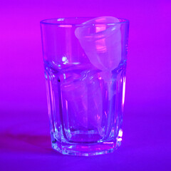 two pink menstrual cups in a glass cup on a purple background photo