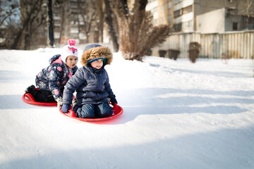 Fototapeta na wymiar Little boy and girl moving from snowy hill on snow sled in winter